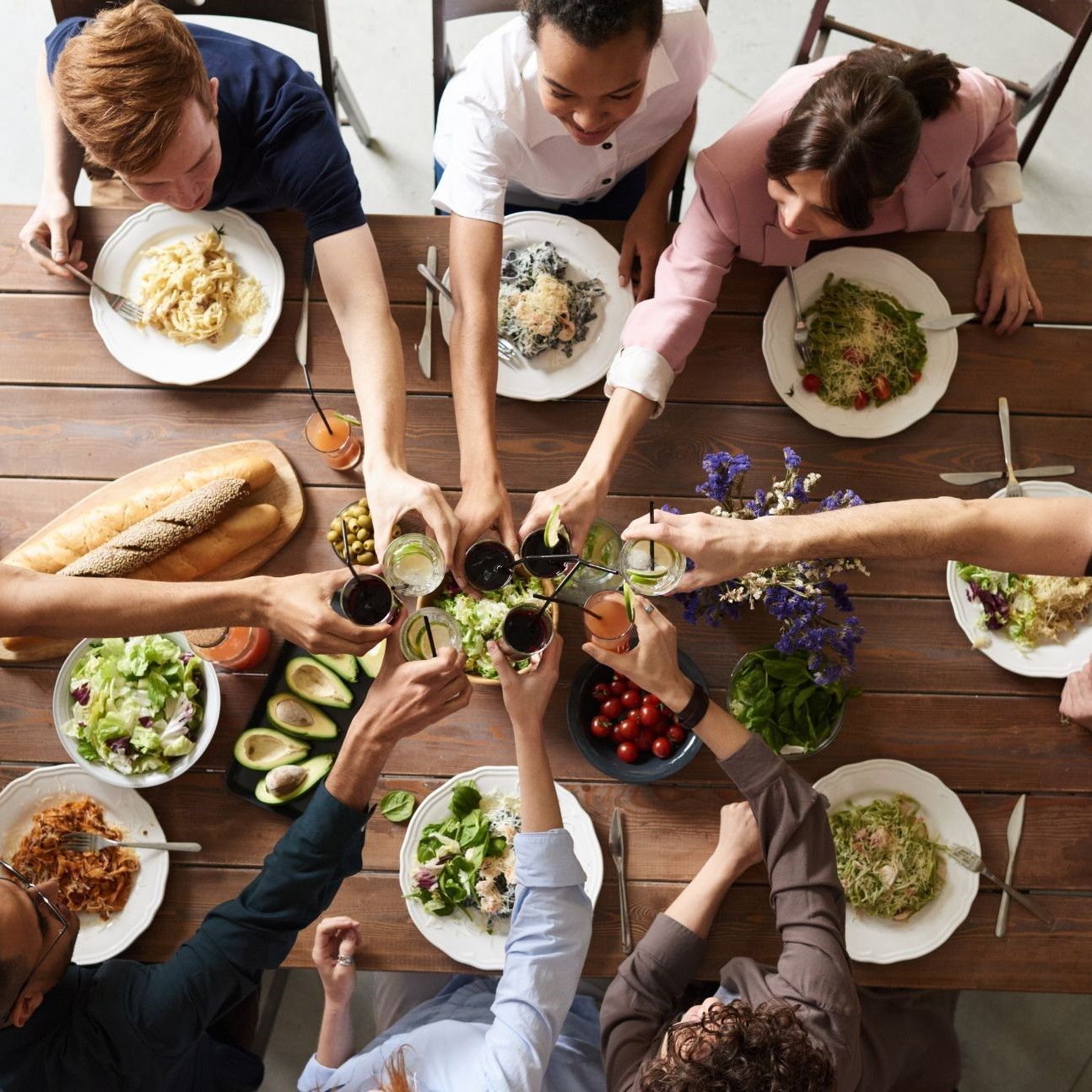 People at a table raise glasses, surrounded by plates of food, vegetables, and bread.