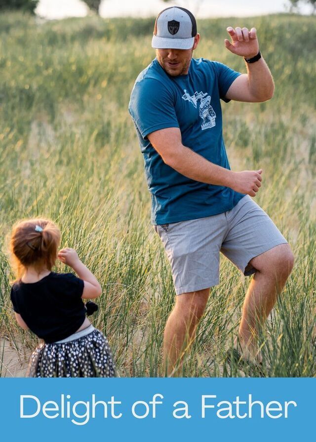 A person and a child dance together in a grassy field during a sunny day. Below them, the text reads