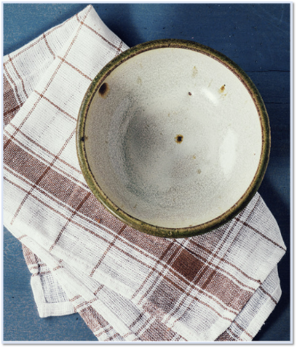 A white ceramic bowl with a dark, textured rim sits on top of a brown and white plaid cloth against a blue background.