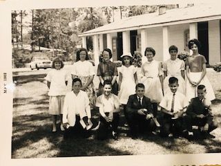 Group of teens posing outside a white building. The teens are smiling and dressed up, likely for a special occasion.