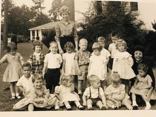 Group of young children with a teacher posing outdoors in front of a building.