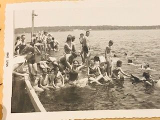 People in swimwear on and around a wooden dock, some in the water. May 1948.