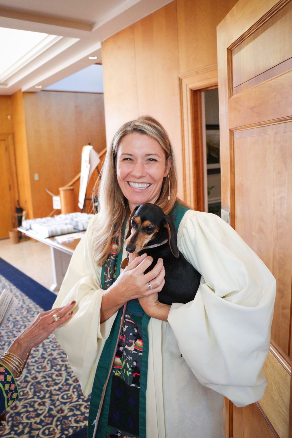 Woman in cream robe holds a small black dog, smiling in a doorway.