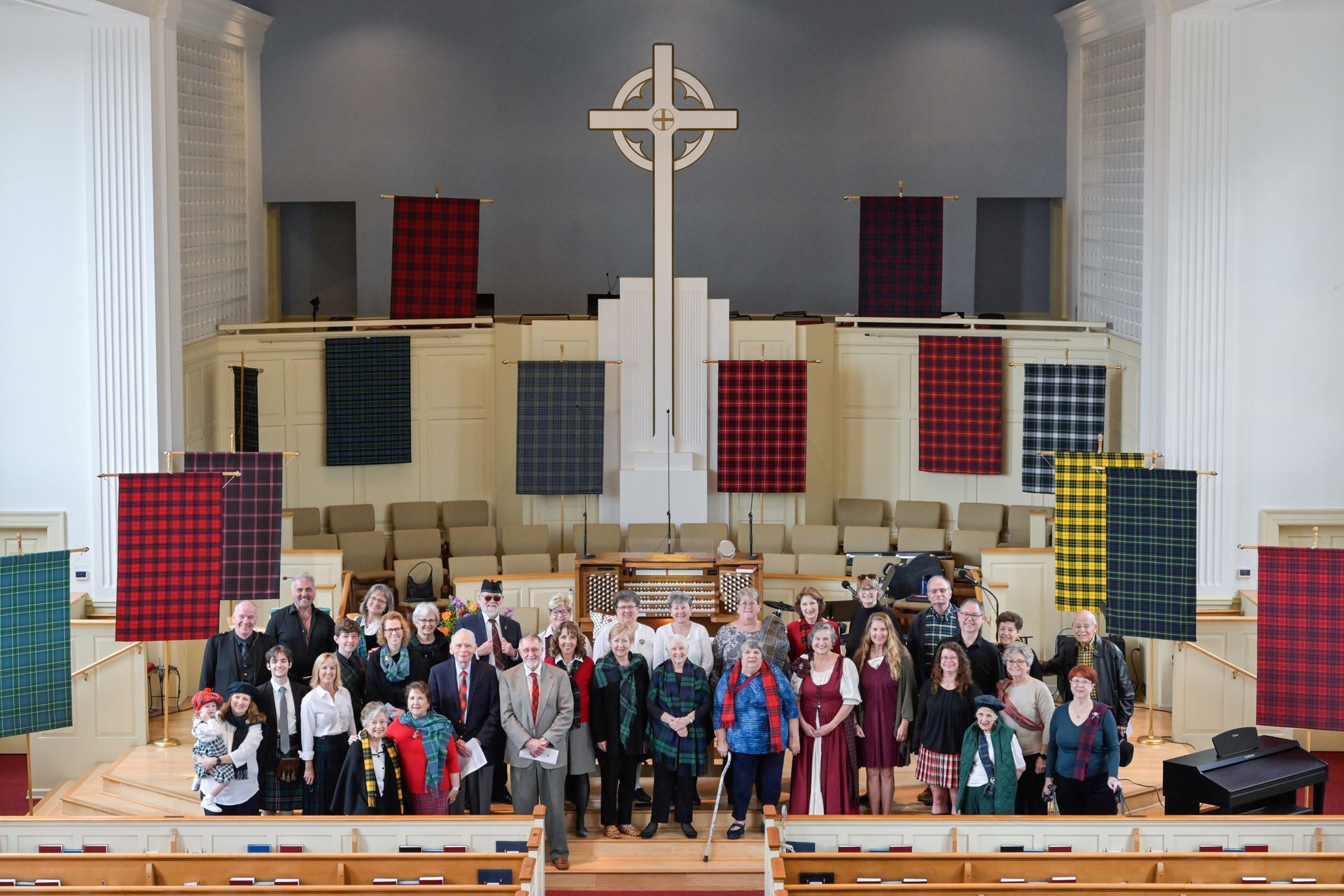 Group of people in a church with a large cross, tartan banners, and an organ.