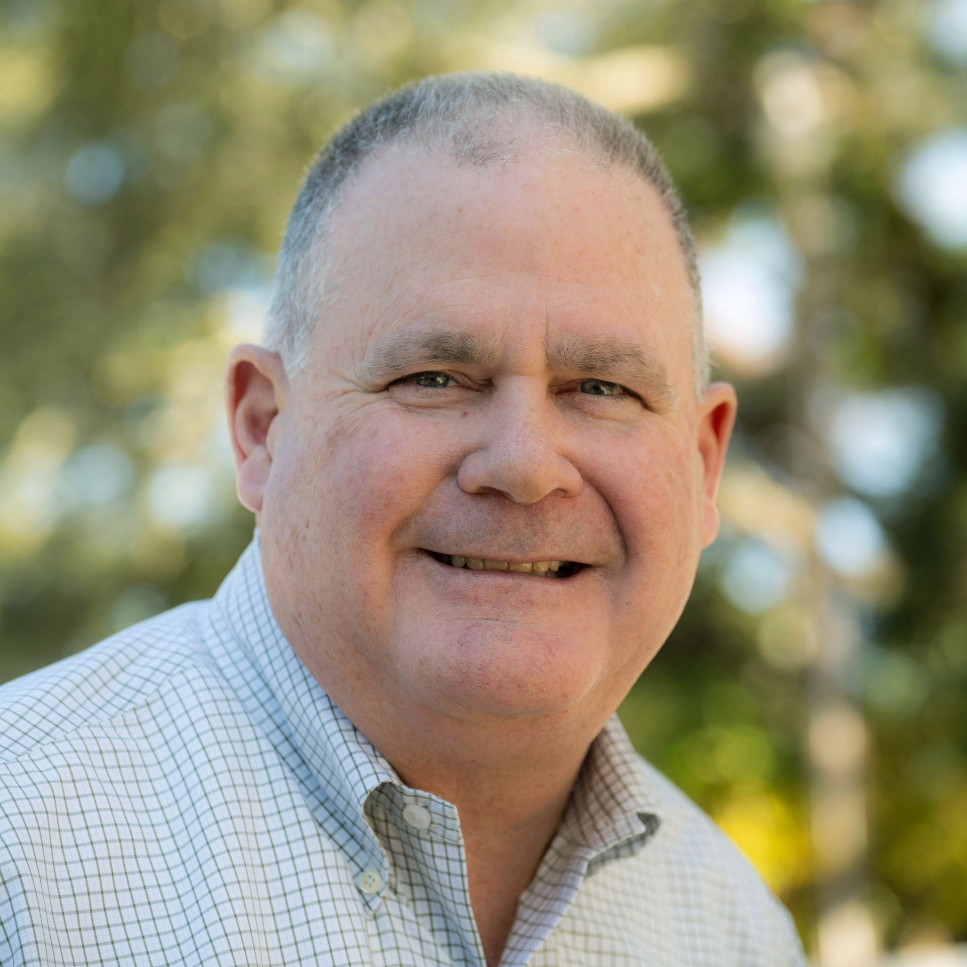 Smiling man with thinning hair wearing a button-down shirt outdoors.