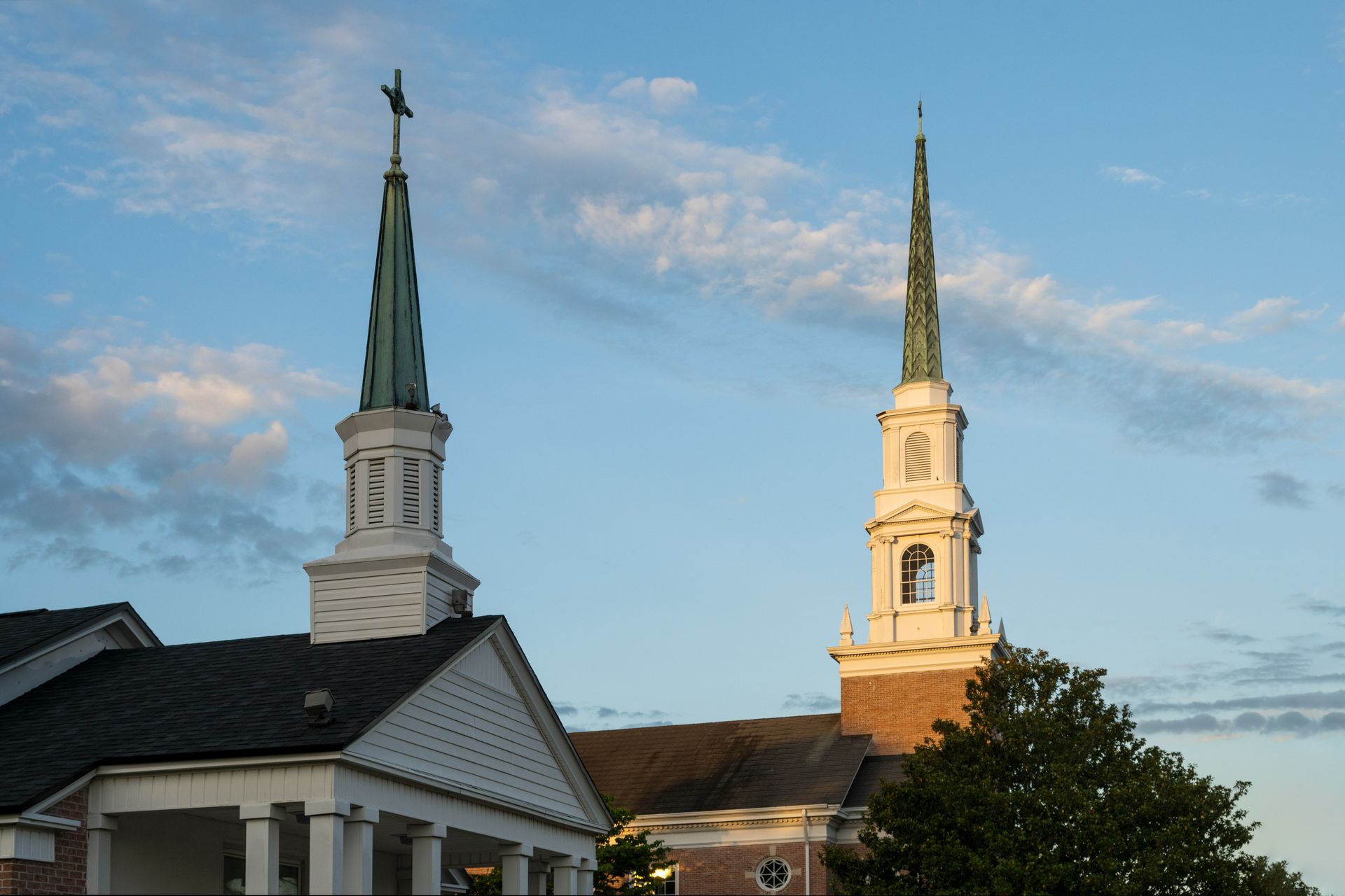Two church steeples rise against a blue sky with soft, scattered clouds during a sunny day.