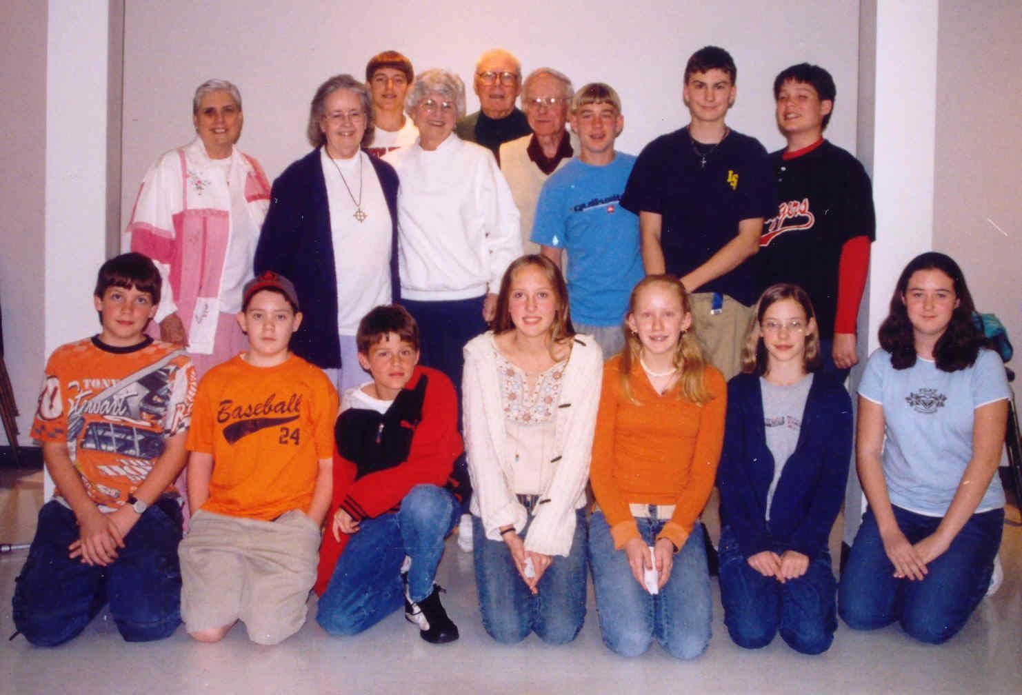 Group of people posing for a photo indoors. Some kneeling in front, others standing behind. White background.