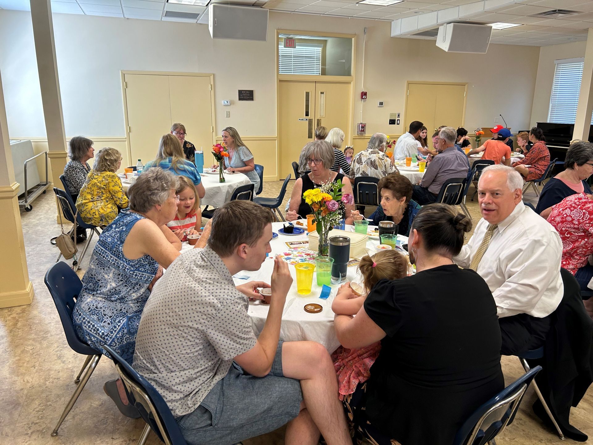 People seated at round tables in a brightly lit room, socializing during an event.