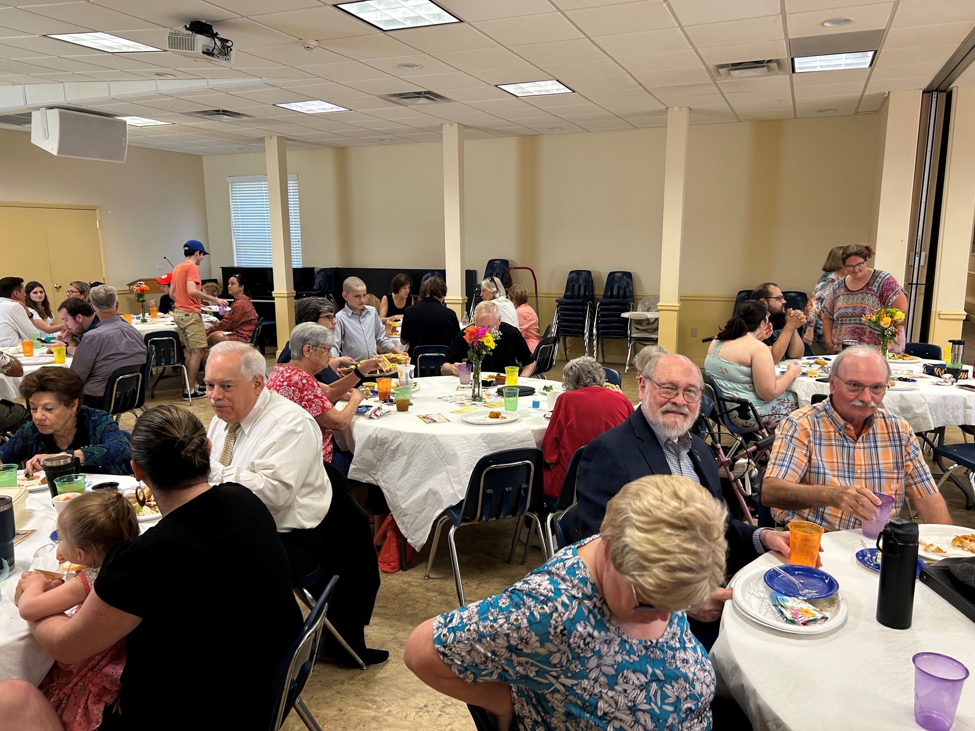 People eating at round tables in a brightly lit room; event or gathering.