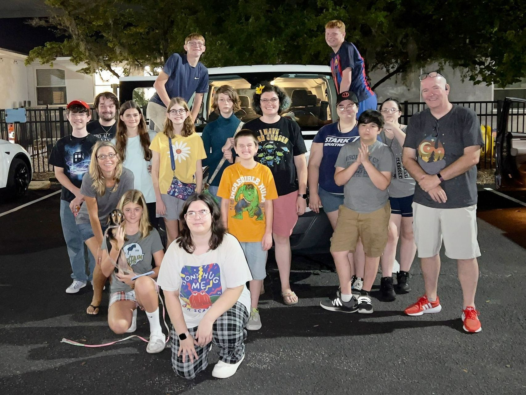 Group of people posing in front of a van at night. Some standing on the van. Smiling and looking at camera.