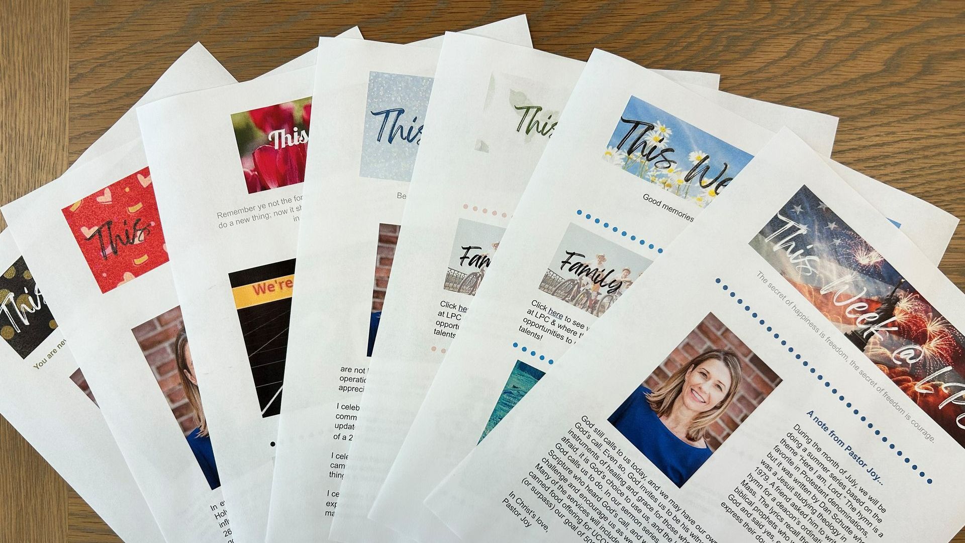 Pile of printed newsletters with colorful headers and a woman's photo, fanned out on a wooden table.