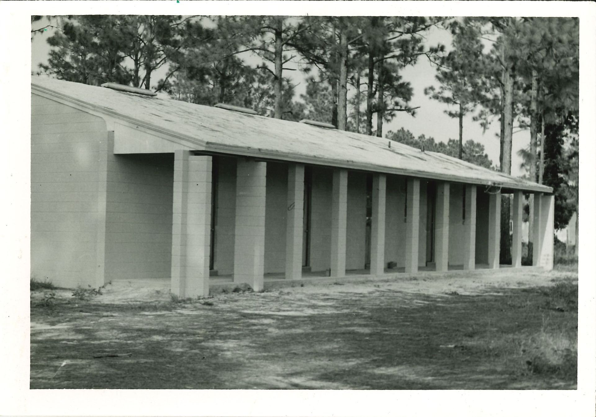 Black and white photo of a long, low building with a covered walkway supported by pillars.