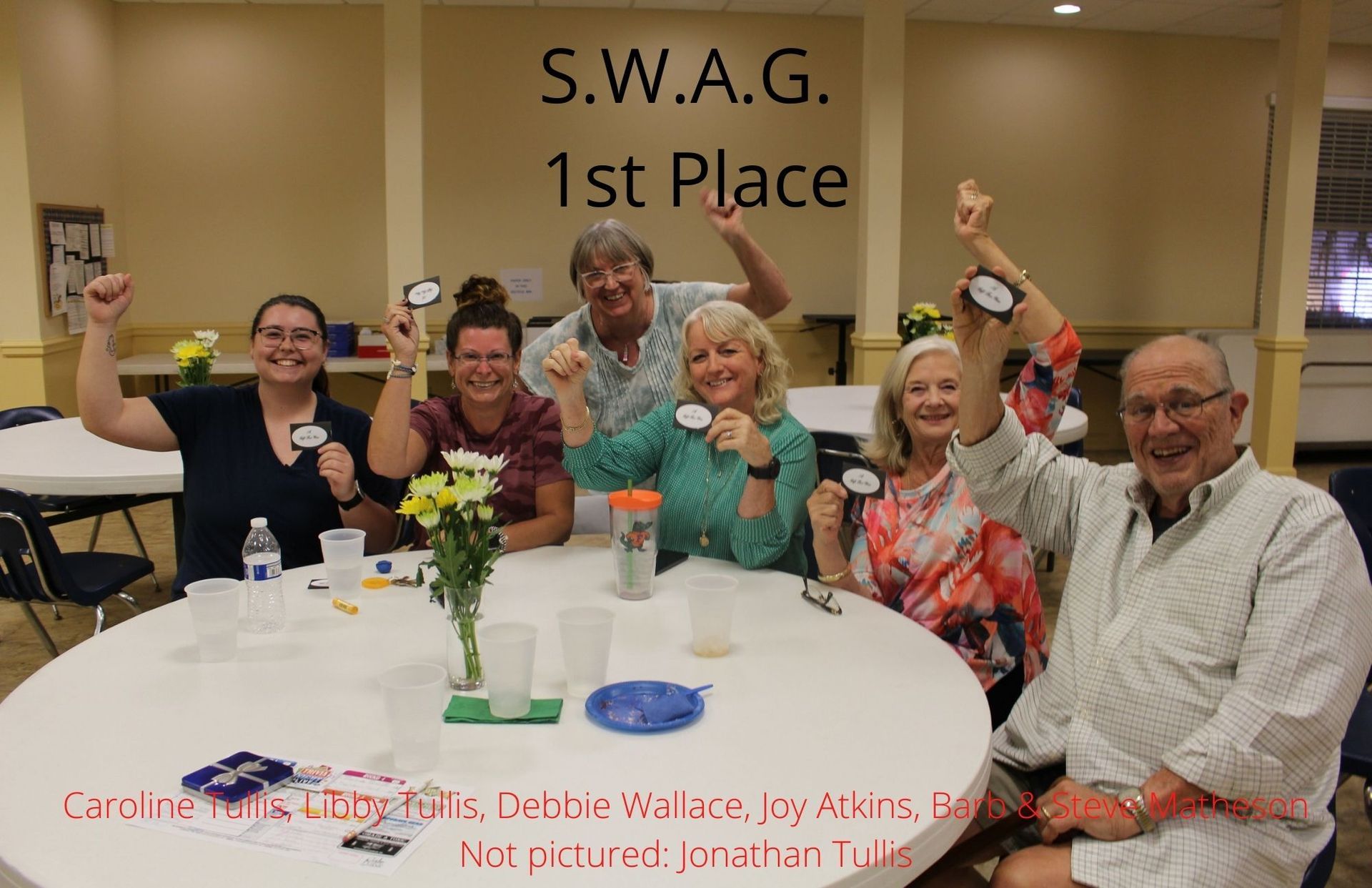 Group celebrates a win at a table, holding awards. 