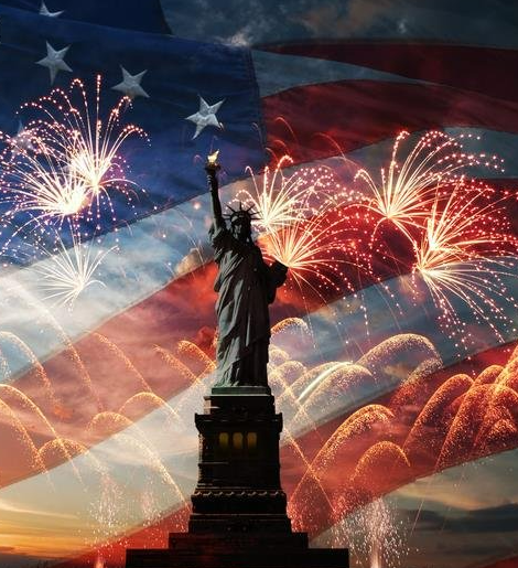 Statue of Liberty silhouetted against an American flag and fireworks at sunset.