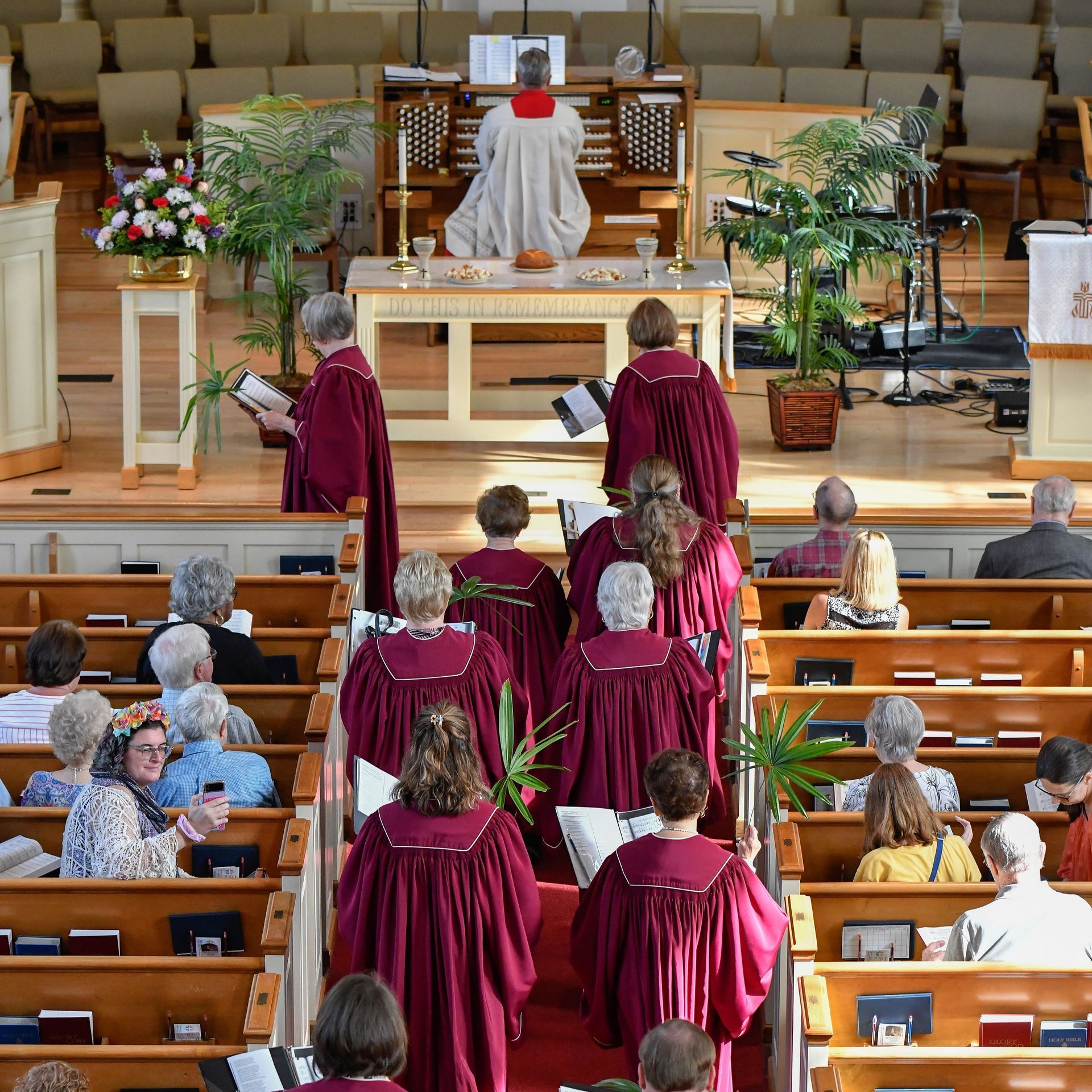 Choir members in burgundy robes walk down the aisle in a church during a service.