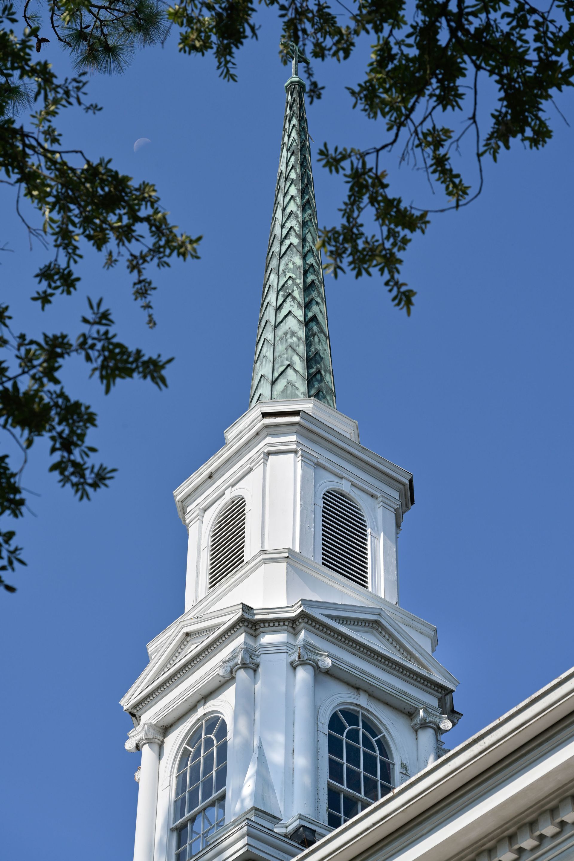 White church steeple against blue sky, framed by tree branches.