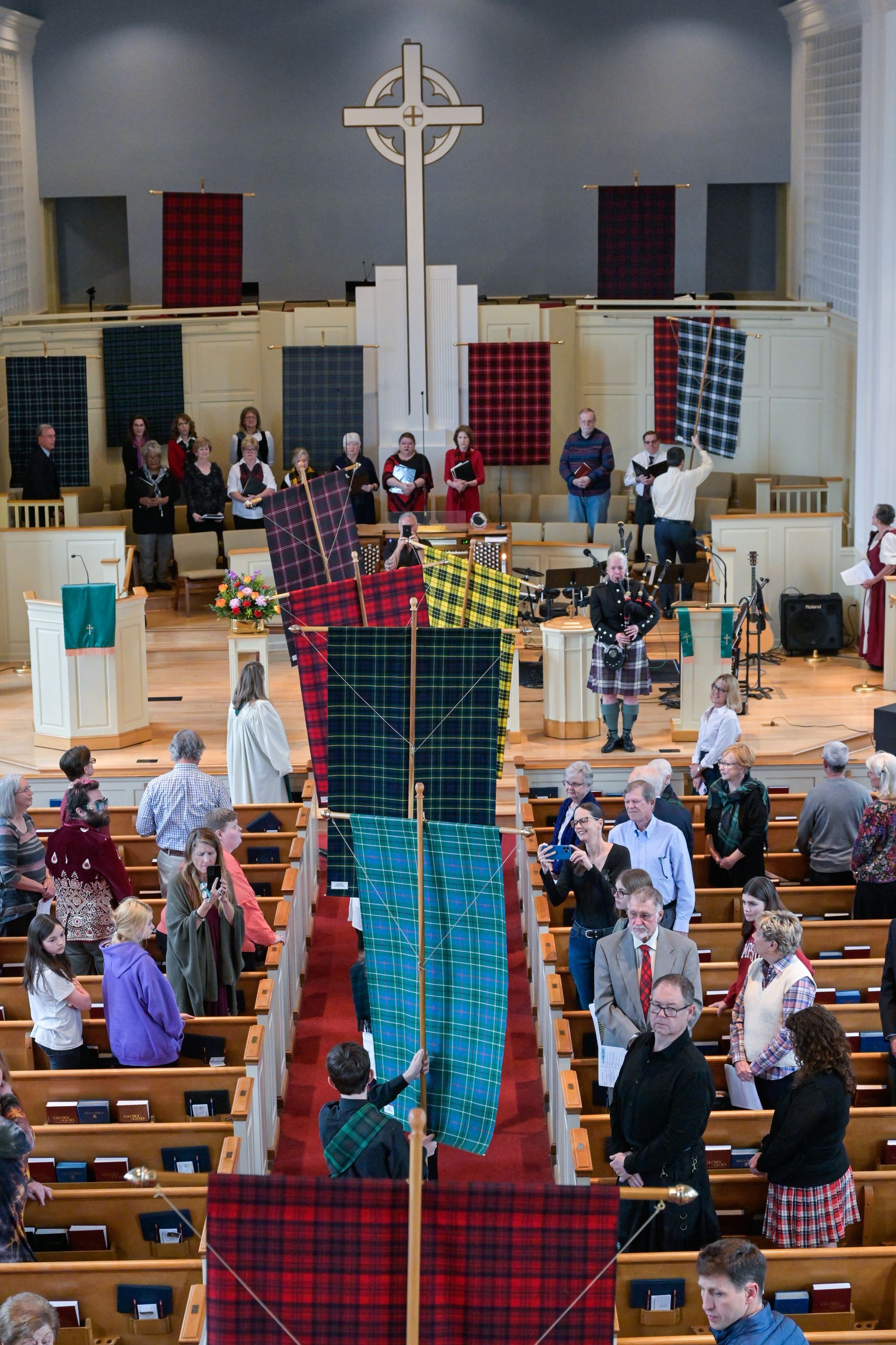 People in a church celebrate a Scottish heritage event. Tartan banners, cross, people in kilts.