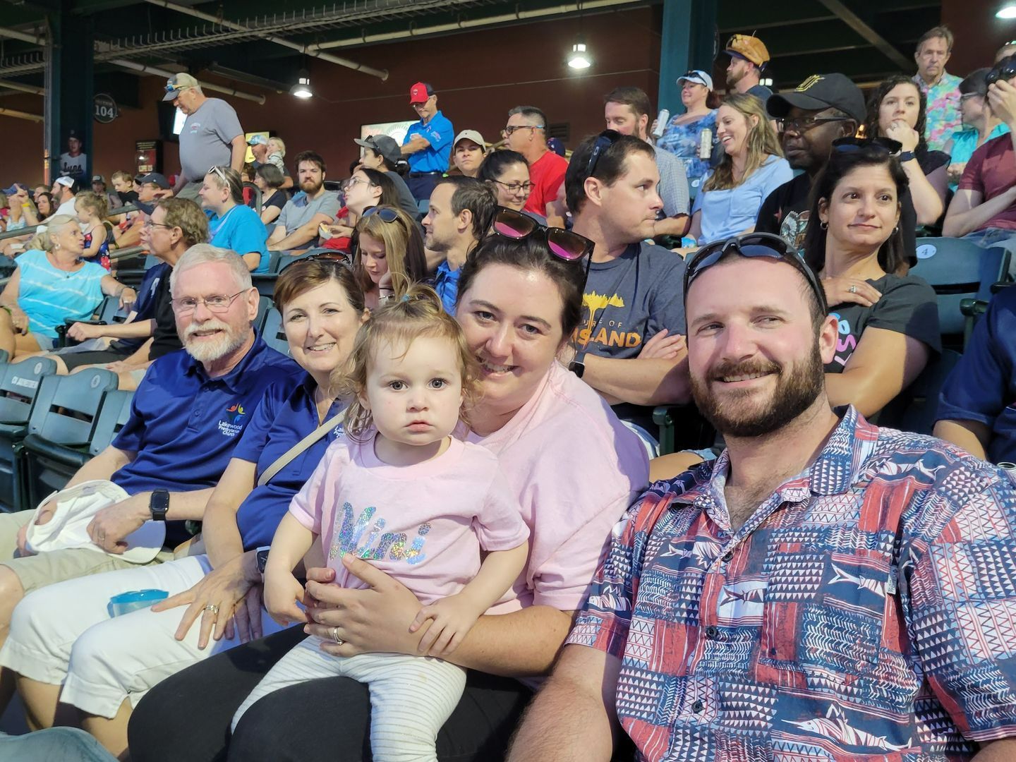 People seated in stadium watching an event; one woman holds a toddler. Other spectators in background.