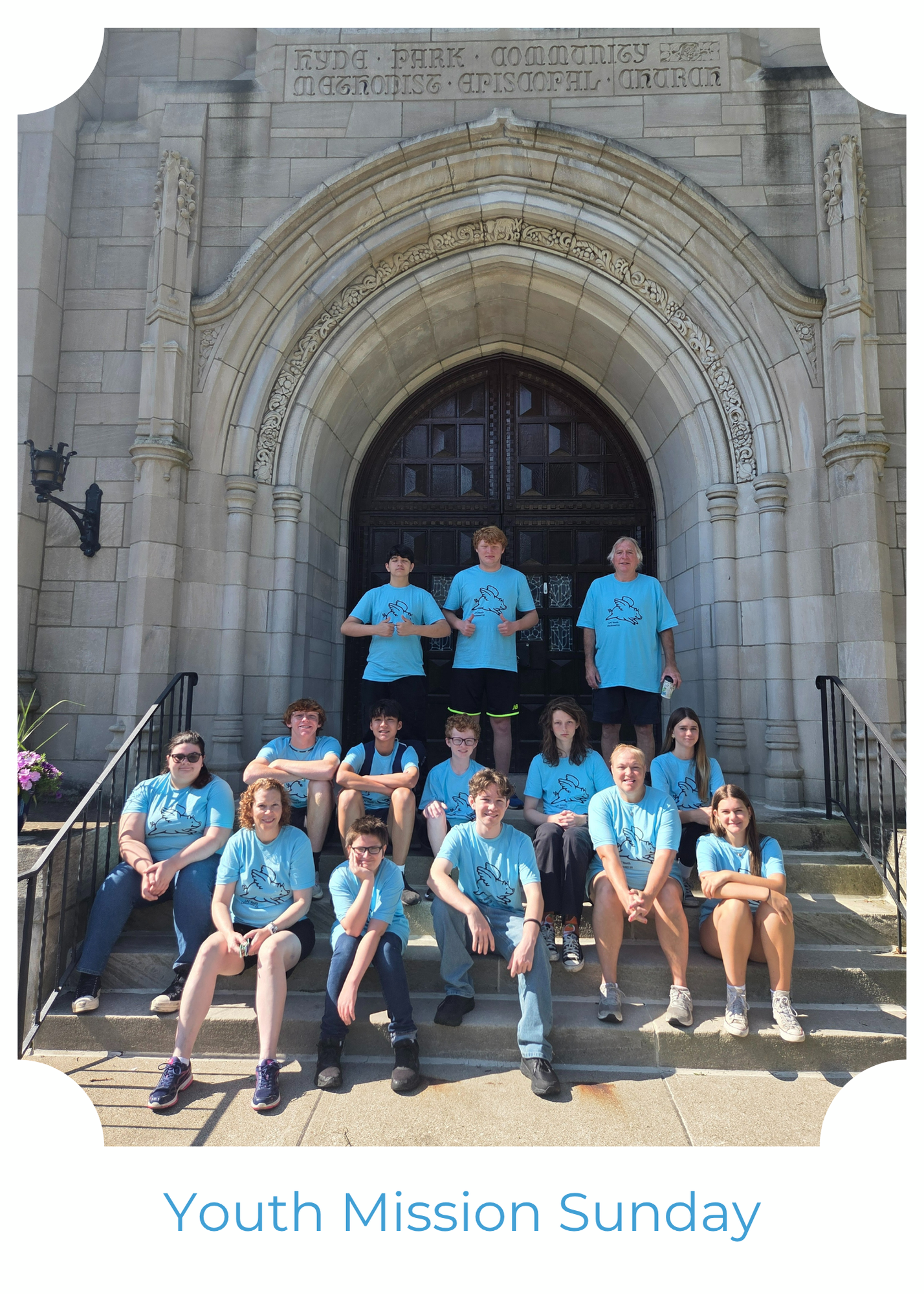 A group of people in matching light blue t-shirts sit and stand on the steps of a stone church building.