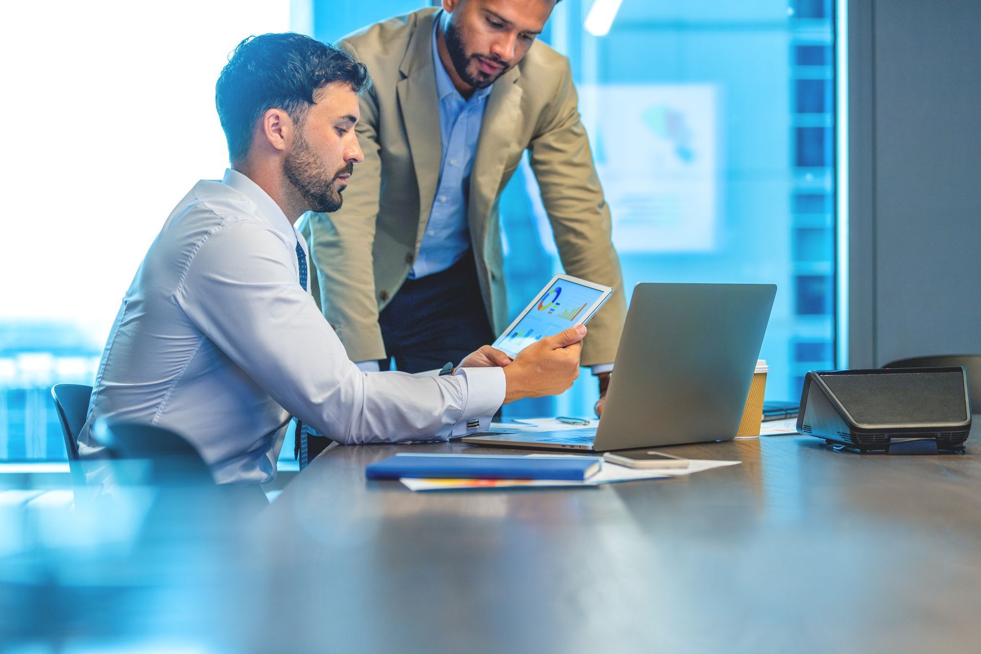 Two men are looking at a laptop computer in a conference room.