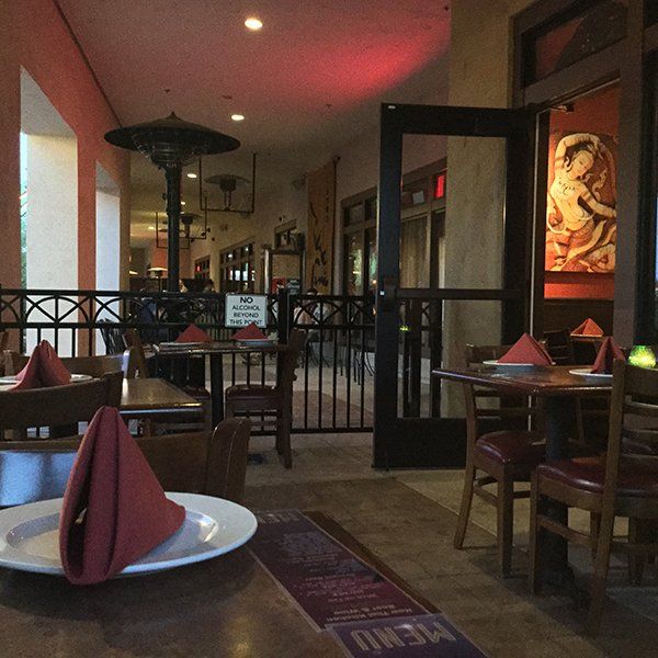 Outdoor restaurant seating; tables set with red napkins and plates. A heater hangs overhead.