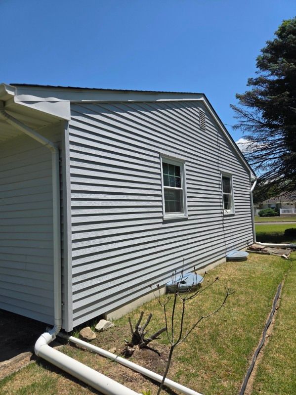 White vinyl-sided house exterior with two windows, downspout, and small yard under a clear blue sky