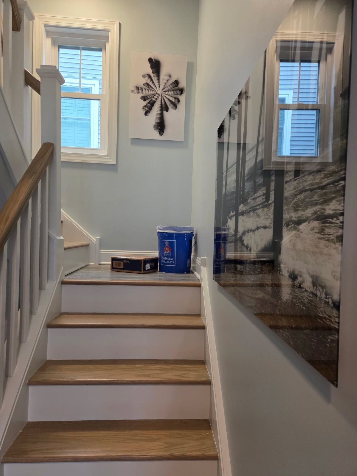 Narrow stairway landing with framed art, blue cooler, windows, and a large wall photograph on the right.
