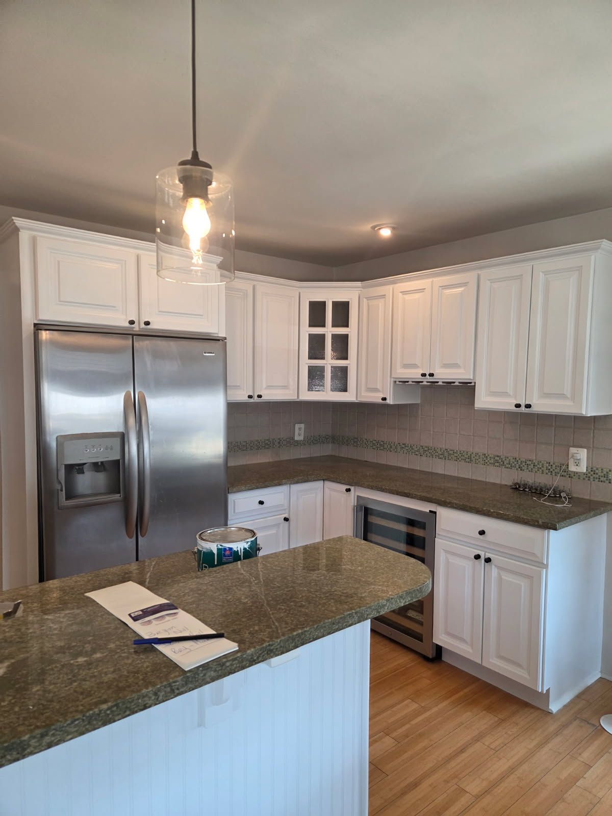 Bright kitchen with white cabinets, stainless steel refrigerator, granite island, and wood floors