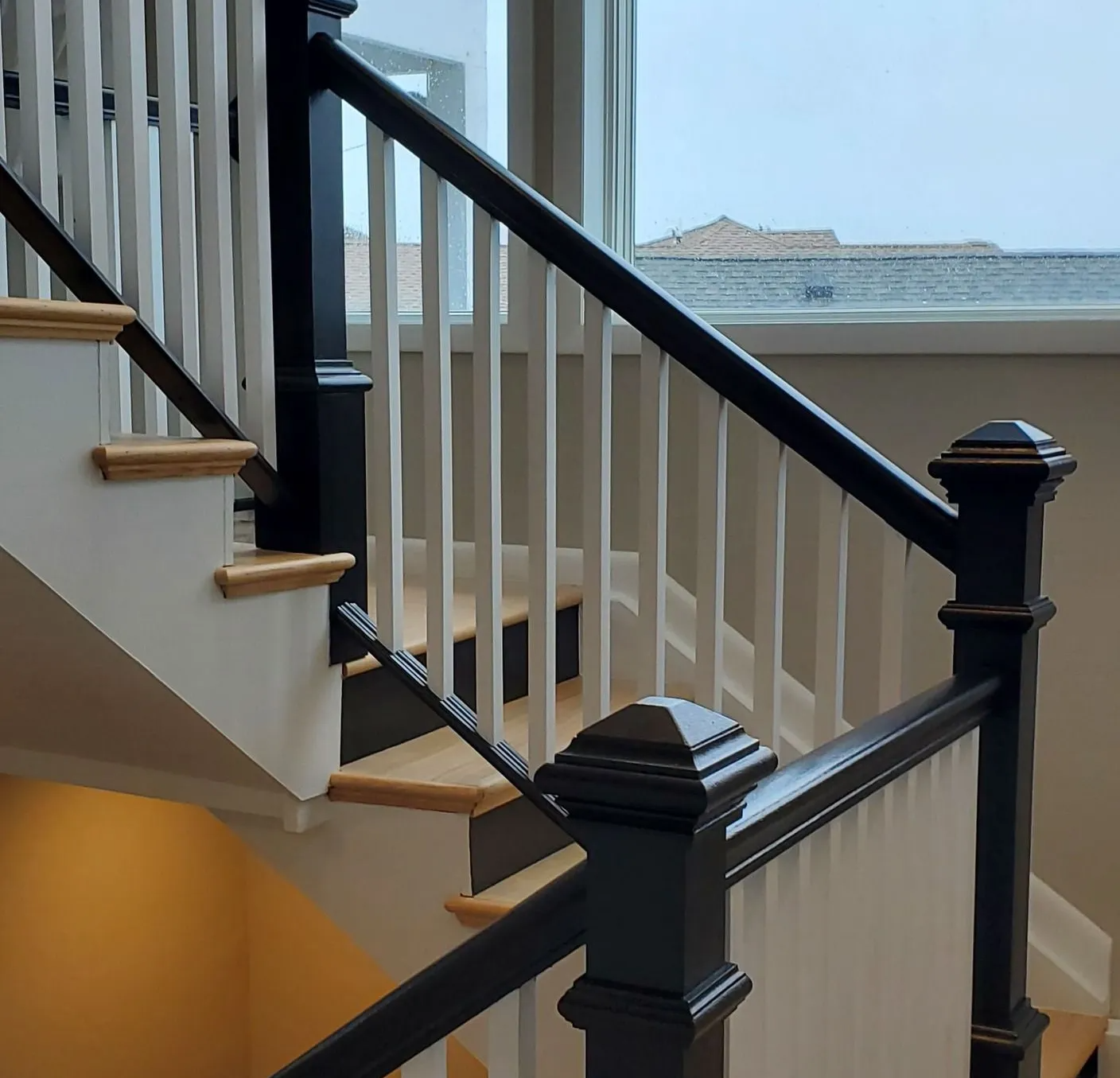 Indoor staircase with black railings and white balusters beside a window