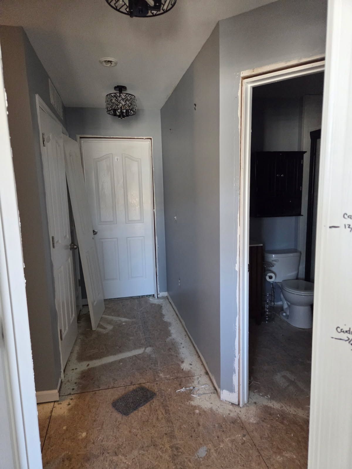 Narrow hallway with unfinished flooring, white doors, and an open doorway to a bathroom.