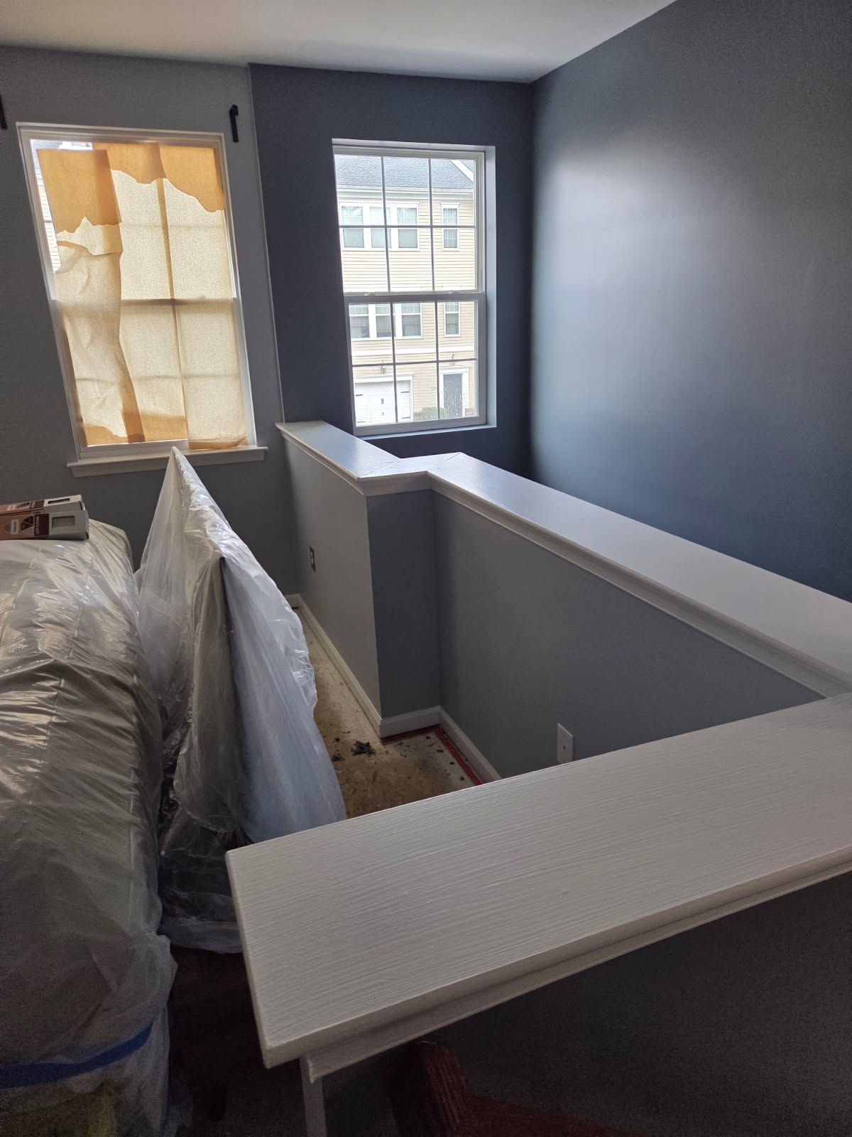 Blue-walled hallway under renovation with plastic-covered furniture and a window at the end