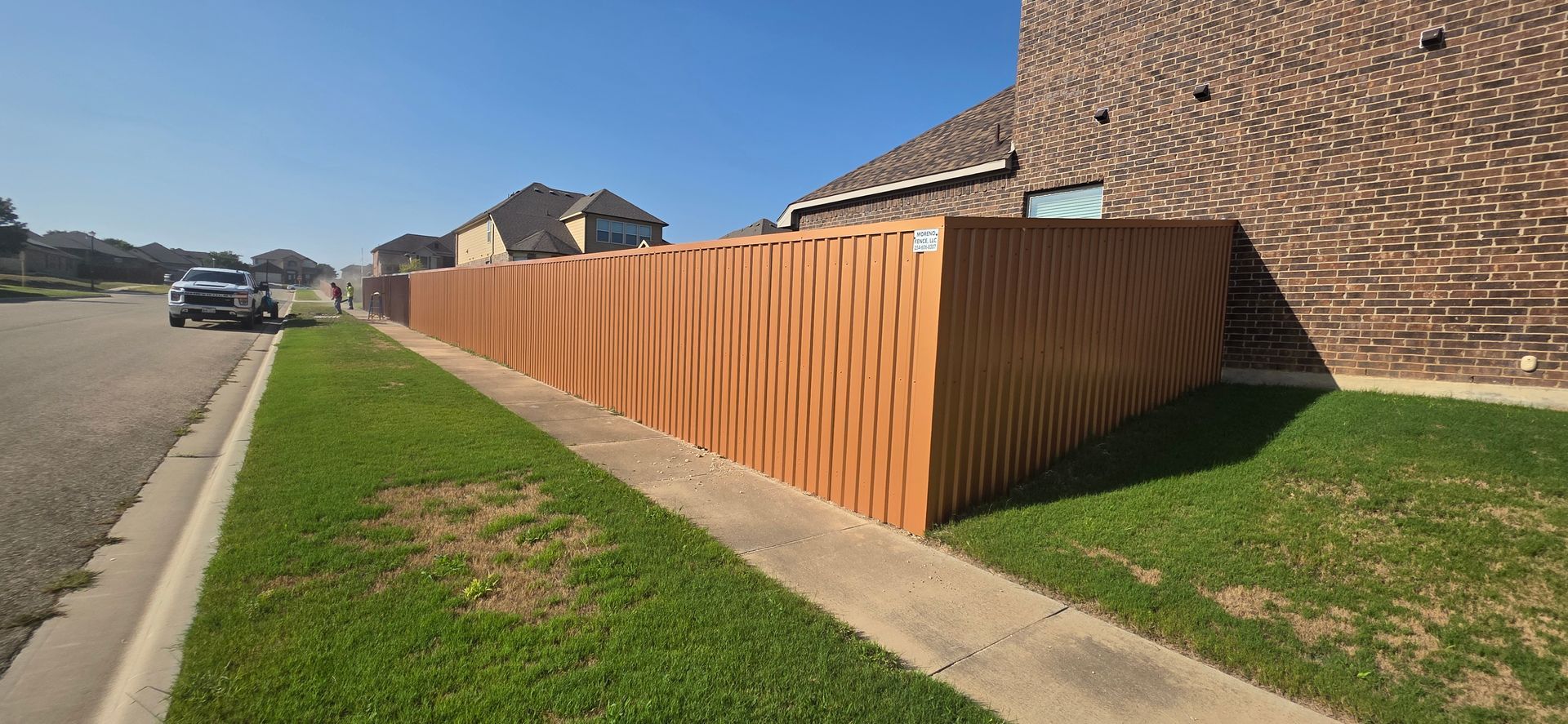 Gloved hand painting a brown metal fence near a gate outdoors