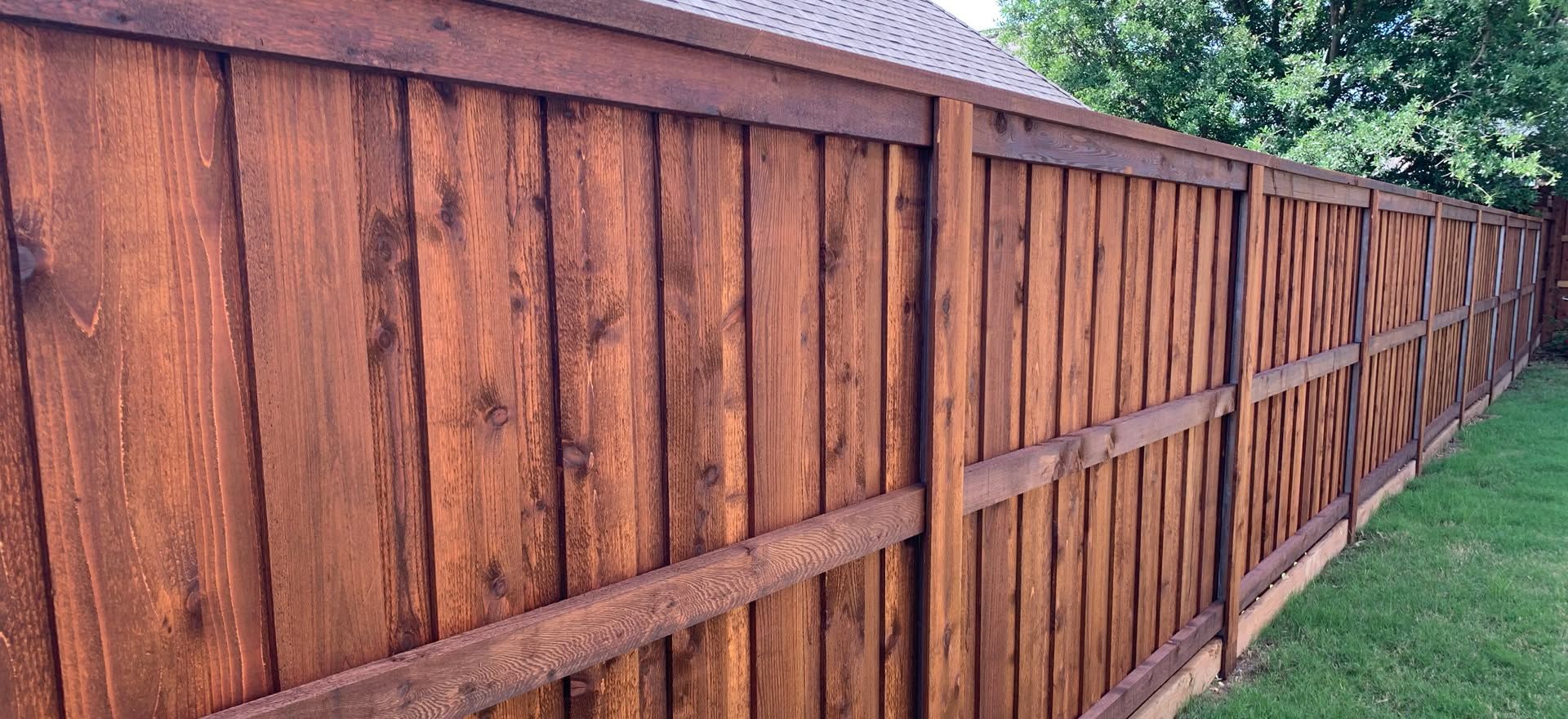 Wooden privacy fence with horizontal supports along a grassy yard