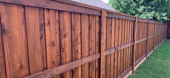 Weathered wooden fence with horizontal rails along a grassy yard on a cloudy day