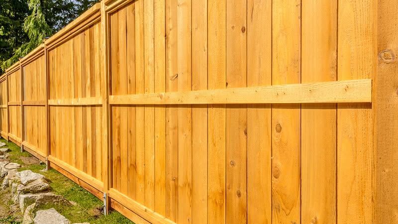 Wooden privacy fence with a horizontal support board along a grassy outdoor path