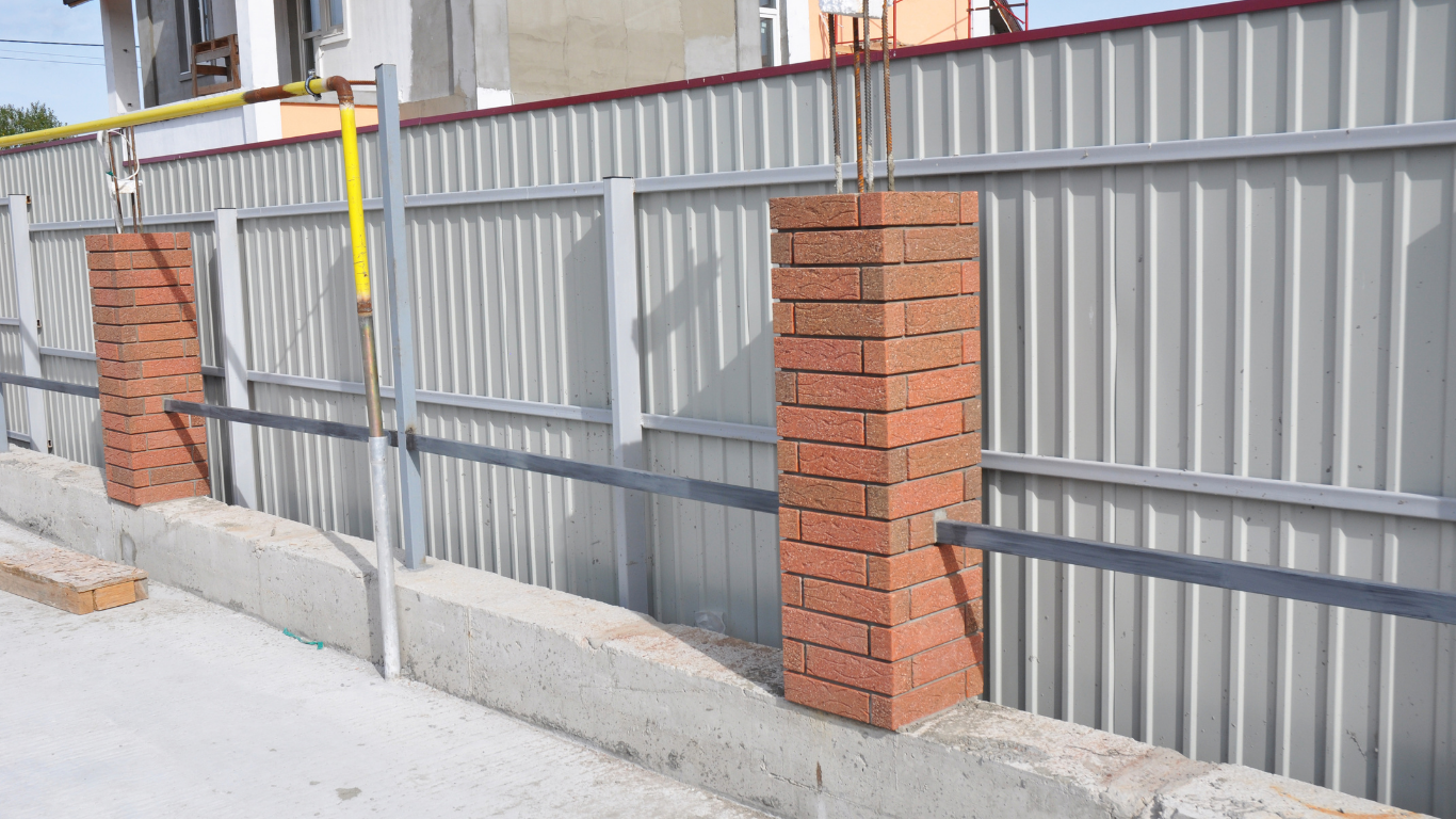 Metal fence with brick pillars beside a concrete sidewalk on a sunny street