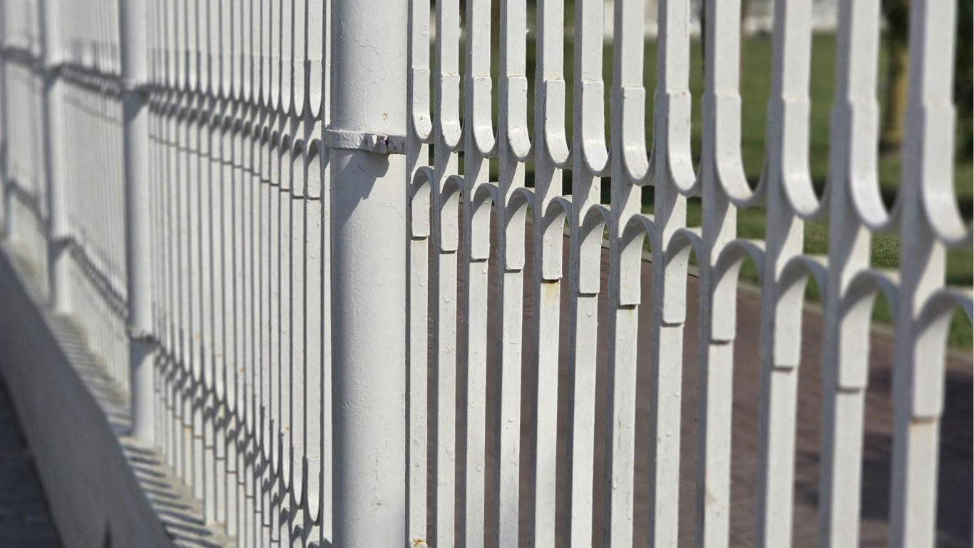 White metal fence with vertical bars along a sidewalk in bright sunlight