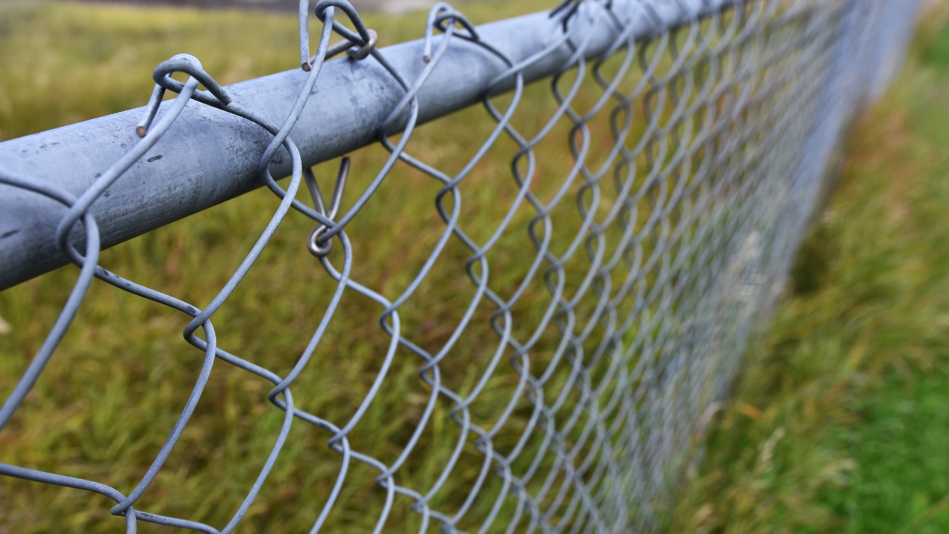 Chain-link fence beside a grassy area, with a gray rail along the top.