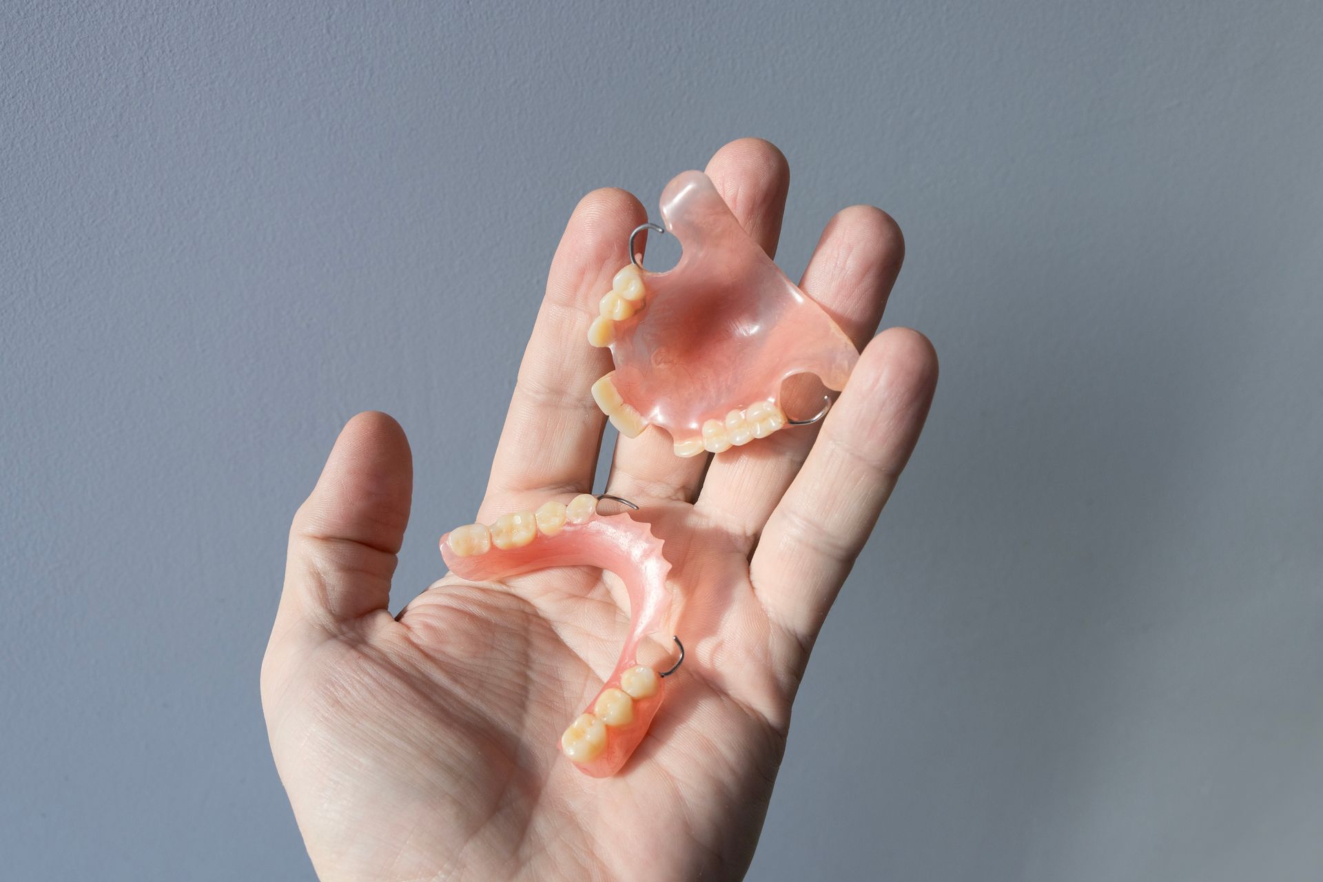 Hand holding a broken set of dentures, against a gray background.