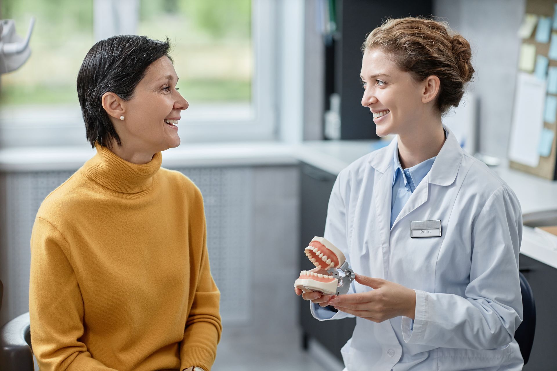Dentist showing teeth model to patient; office setting, both smiling.