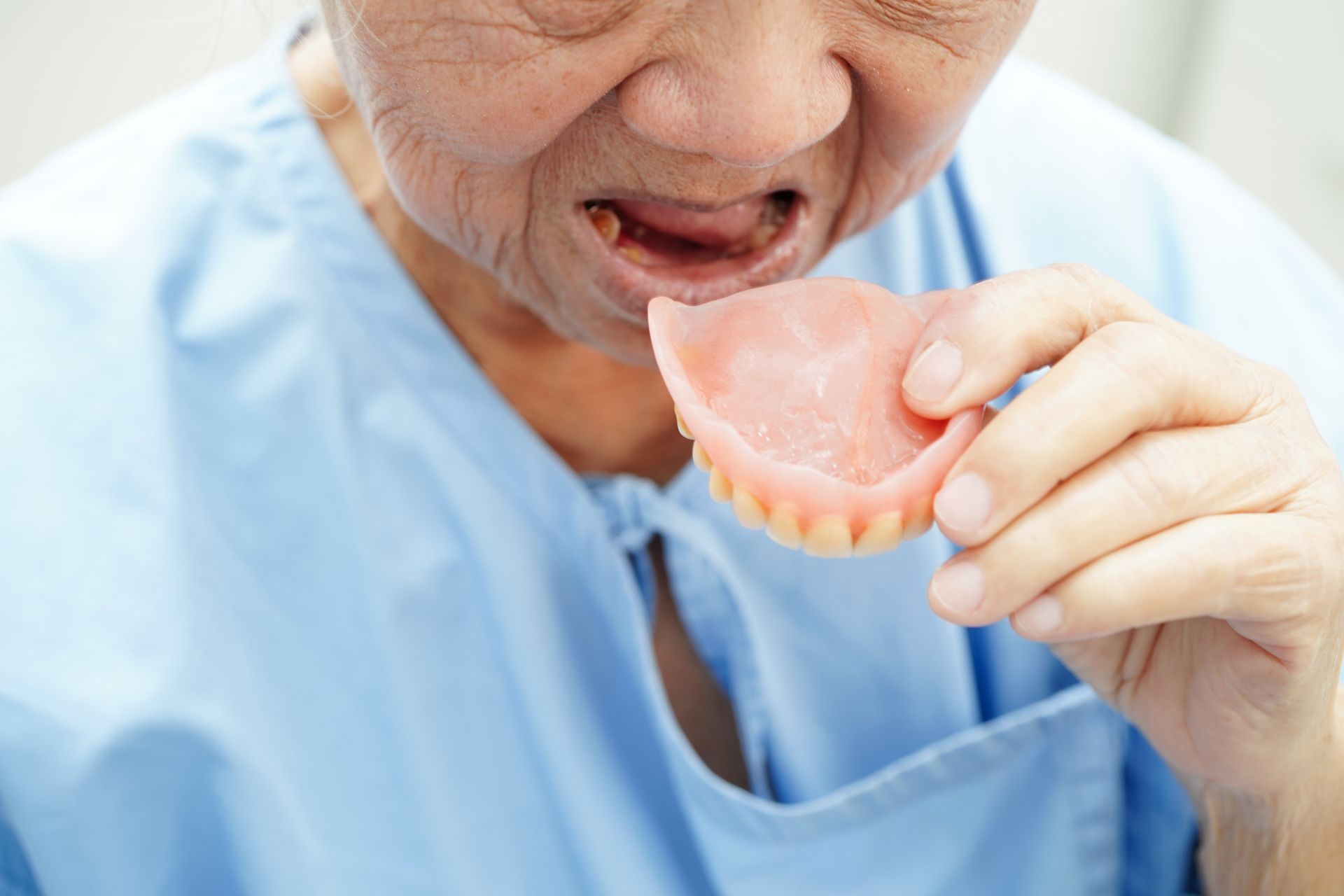 Person holding dentures, preparing to insert them. Pink dentures in focus; pale blue top.