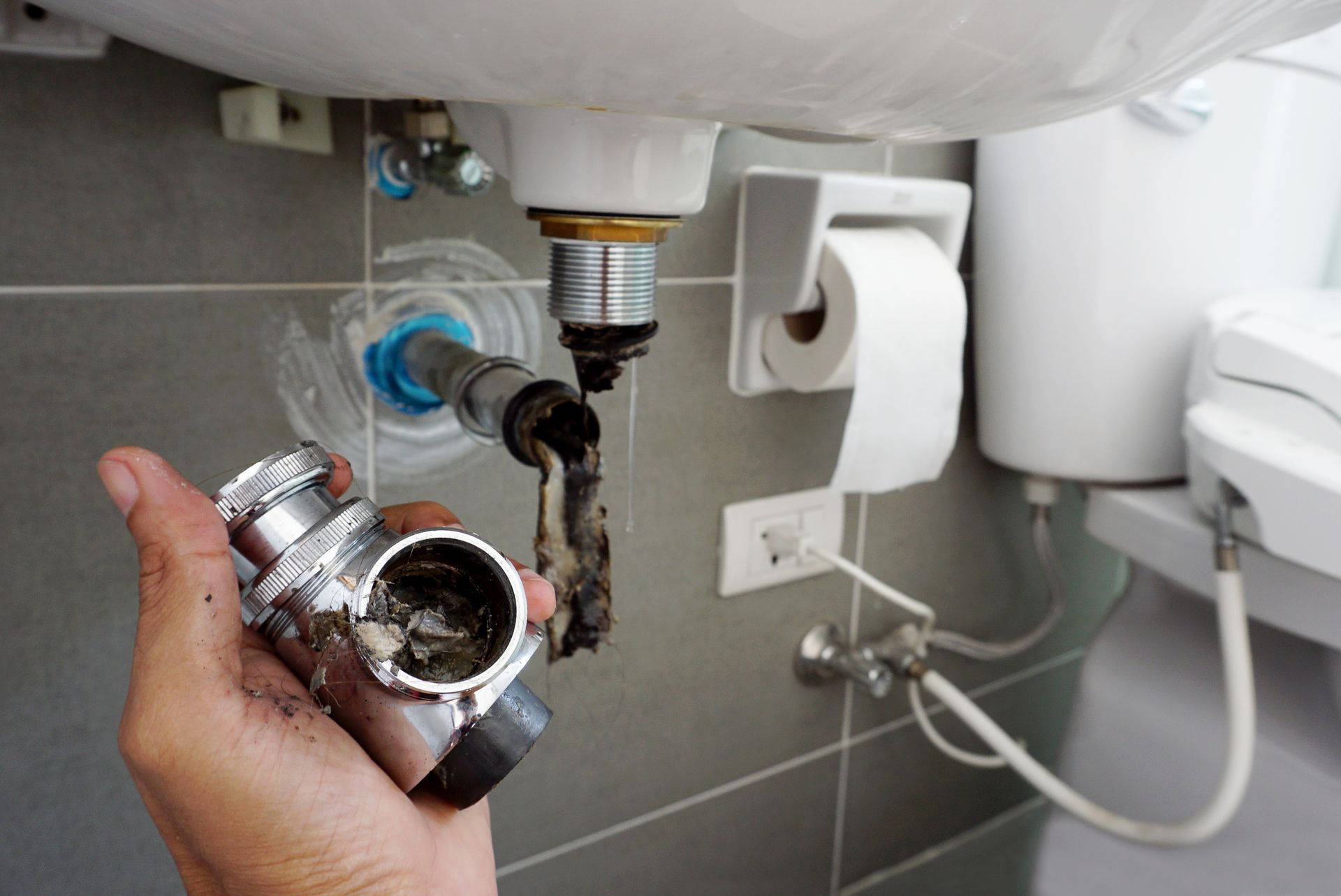 Plumber holding dirty drain trap removed from under bathroom sink.
