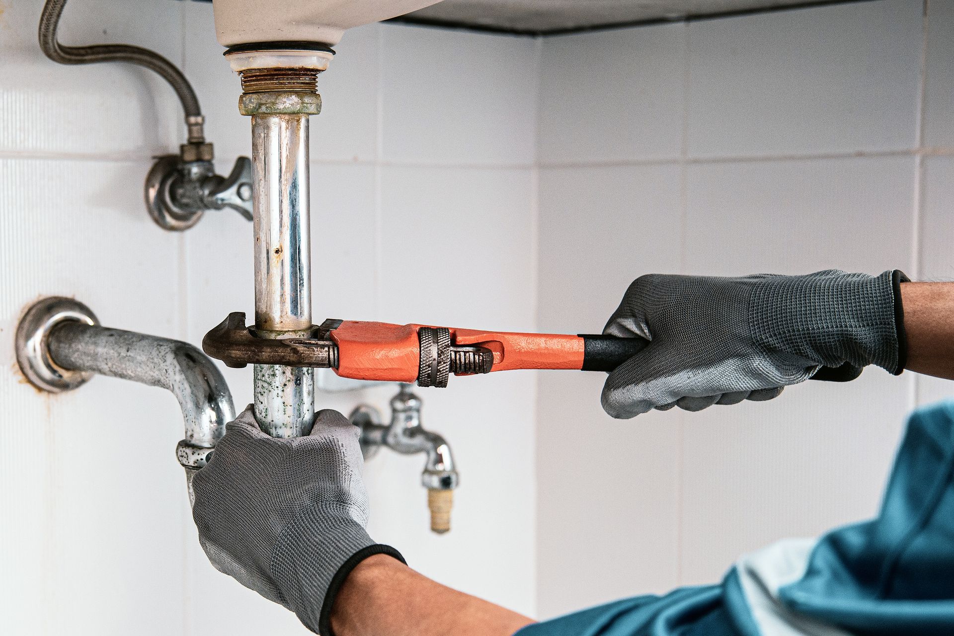Plumber using a wrench to tighten a pipe under a sink. Plumber using a wrench to tighten a pipe under a sink.
