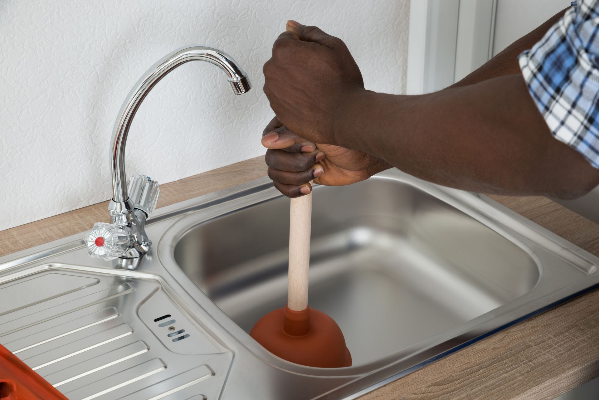 An African male plumber from Calhoun Plumbing cleaning a sink with a plunger for clogged drain clean