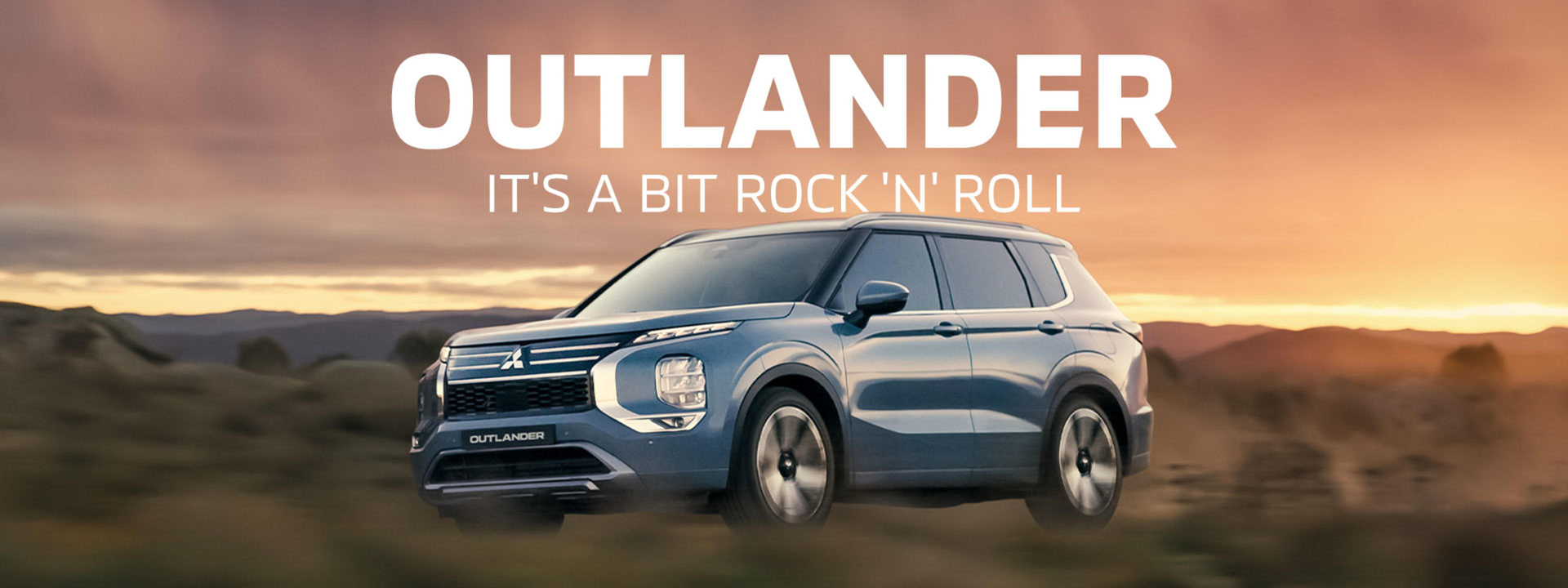 Blue Mitsubishi Outlander SUV driving through a field at sunset. Text reads 