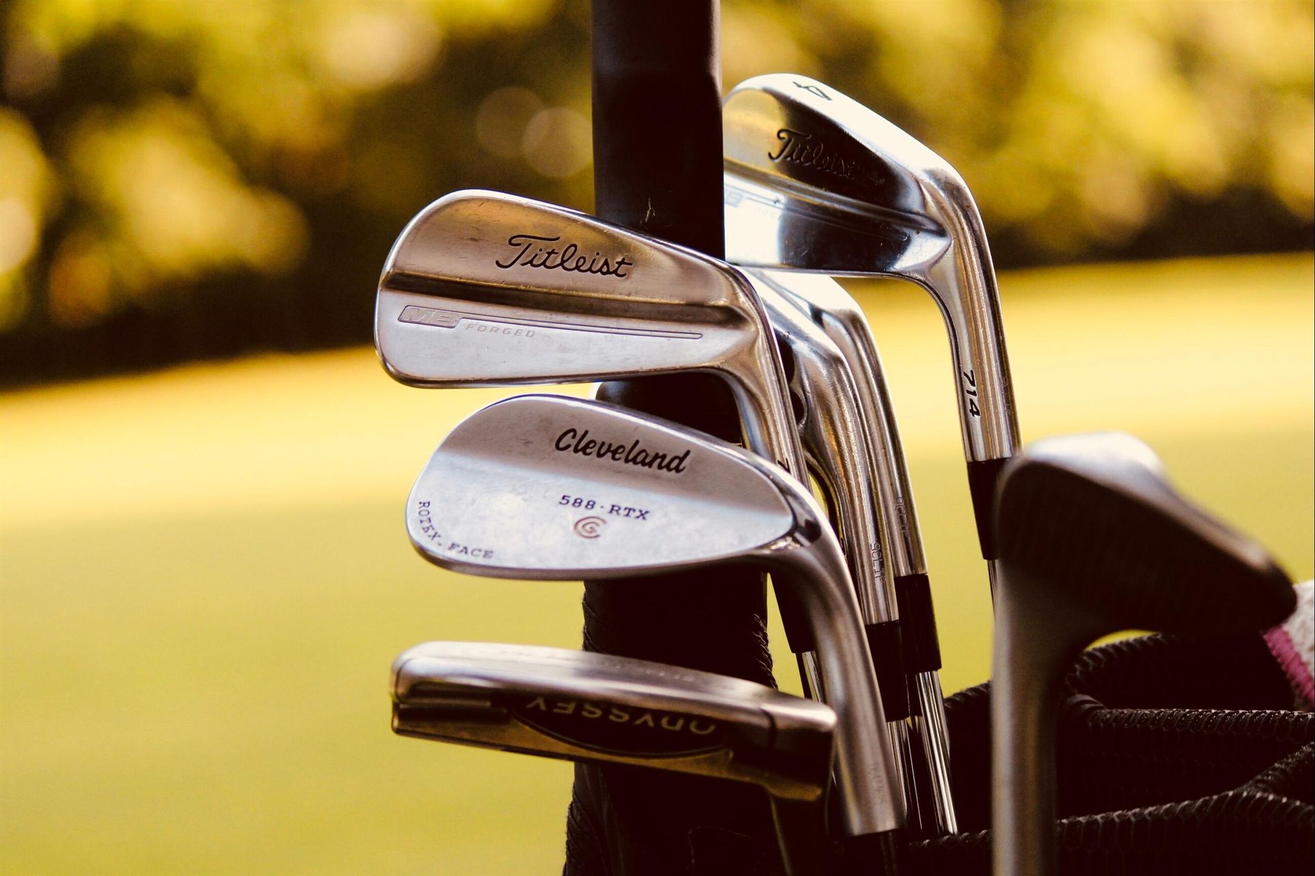A close-up of several golf clubs in a bag, with blurred green grass in the background.