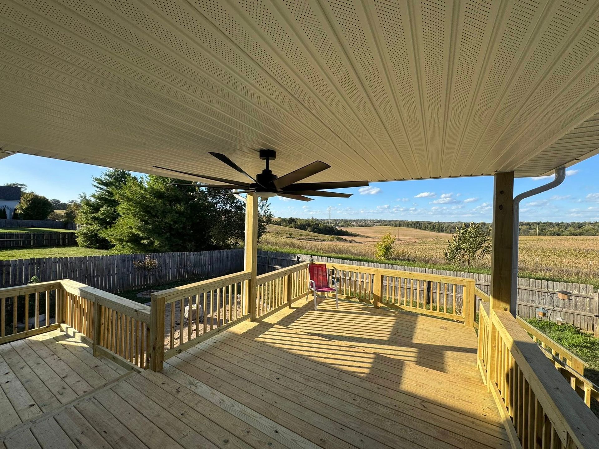 Covered wooden deck with a ceiling fan, overlooking a field.