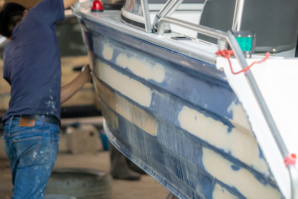 A Man Is Painting a Boat in A Garage — Ashby Boat Builders In Buddina, QLD