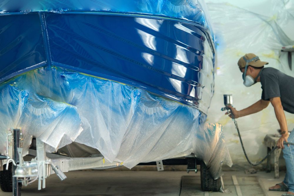 A Man Is Spray Painting a Blue Boat in A Garage — Ashby Boat Builders In Buddina, QLD