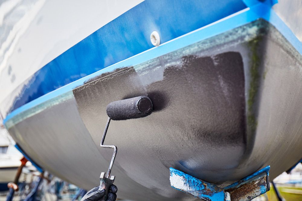 A Person Is Painting a Boat with A Roller — Ashby Boat Builders In Buddina, QLD
